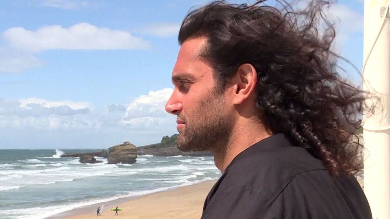 A man with long hair standing on a beach.